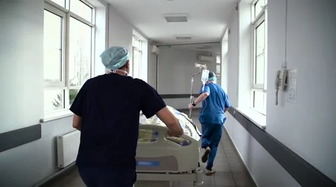 Patient on stretcher pushed at speed through a hospital corridor by doctors Stock Footage