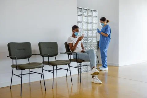 Patient using smartphone while sitting in a waiting room. Stock Photos