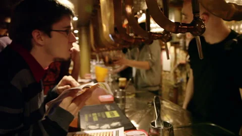 Patrons Reading Menu at Busy Bar Counter with Copper Draft Beer Taps Stock Footage 346638614