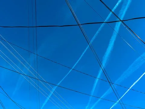 Pattern of airplane contrails and electrical wires over blue sky in spring Stock Photos