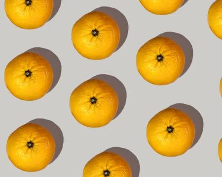 A pattern of big orange mandarins with a pronounced shadow on a beige backgro Stock Photos
