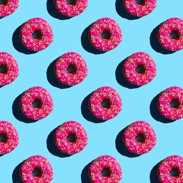 Pattern of donuts in pink glaze sprinkled with colored crumbs on a blue backg Stock Photos