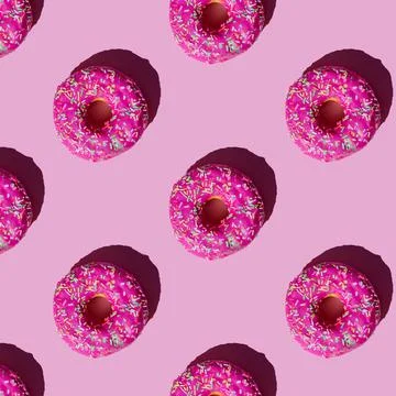 Pattern of donuts in pink glaze sprinkled with colored crumbs on a pink backg Stock Photos