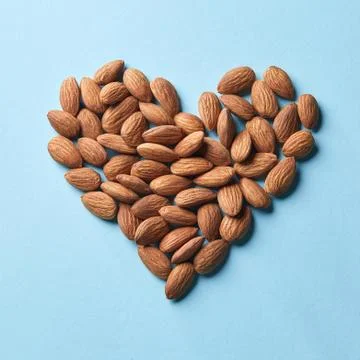 Pattern in the form of heart from almonds on a blue paper background 스톡 사진