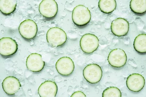 Pattern with freshly cut cucumber slices and ice cubes on green background Stock Photos