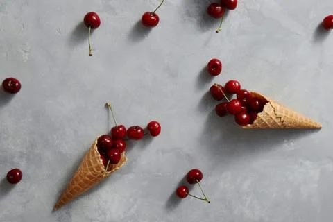 Pattern of freshly picked ripe cherries in a sweet wafer cones on a gray Stock Photos