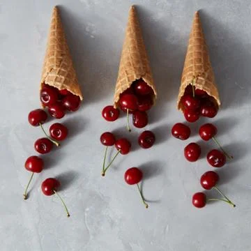 Pattern of freshly picked ripe cherries in a sweet wafer cones on a gray Foto stock