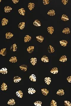 A pattern of golden confetti in the shape of a monstera leaf on a black backg Stock Photos