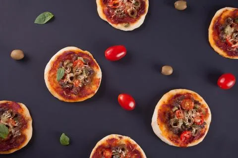 Pattern with homemade mini pizza, cherry tomatoes and green olives on the bla Stock Photos