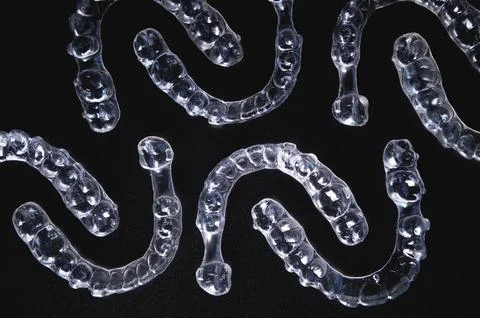 A pattern of invisible plastic aligners lie on a black background Stock Photos
