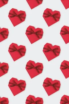 Pattern made of red gift box in a heart shape with tied glittering ribbon. Stock Photos