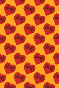 Pattern made of red gift box in a heart shape with tied glittering ribbon. Stock Photos