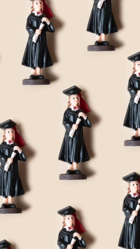 Pattern made from statuette in black graduate hat and gown on beige background Stock Footage 239003544