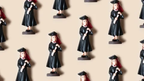 Pattern made from statuette in black graduate hat and gown on beige Stock Footage 239003561