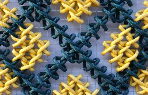 A pattern of multicolored woven ropes set against a metal mesh. Stock Photos