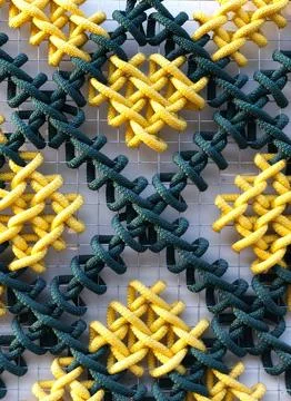 A pattern of multicolored woven ropes set against a metal mesh. Stock Photos