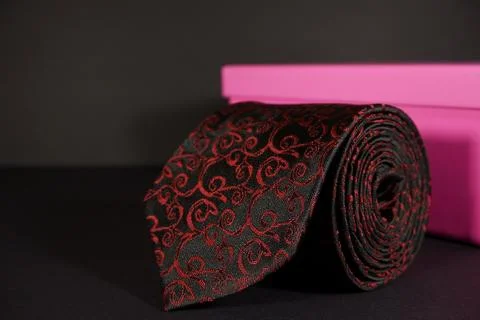 Pattern polyester fabric necktie rolled isolated over black background with gift 스톡 사진