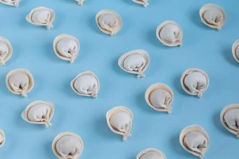 A pattern of raw, frozen dumplings on a light blue background. Stock Photos