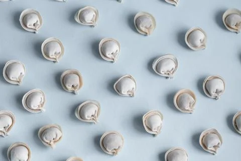 A pattern of raw, frozen dumplings on a light blue background. Stock Photos