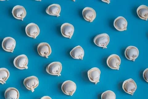 A pattern of raw, frozen dumplings on a light blue background. Stock Photos