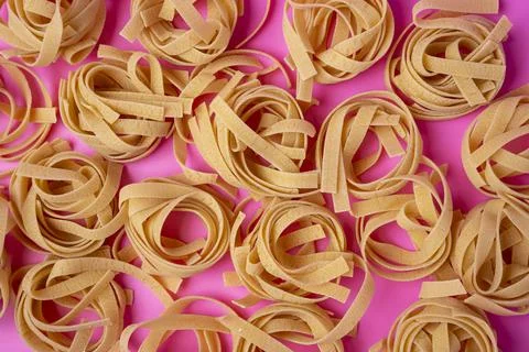 A pattern of Raw tagliatelle on a pink background, pasta nests, egg paste Stock Photos