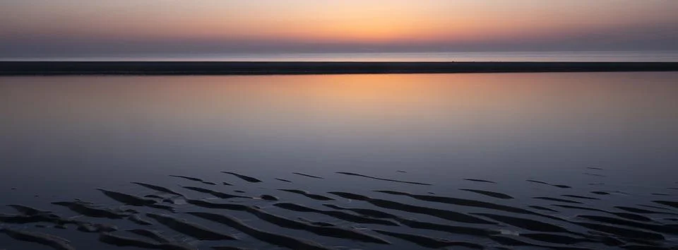 Pattern in sand and colorful reflection of setting sun in water Stock Photos