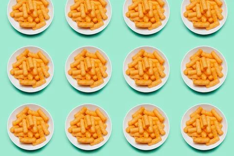Pattern of white round bowls with corn puffs on green background. Stock Photos