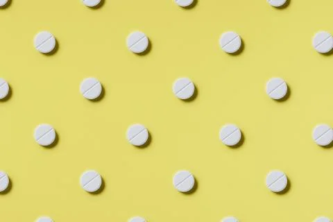 Pattern of white rouned shaped pills on a yellow background. Hard light. Stock Photos
