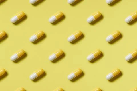 Pattern of yellow and white pills on a yellow background. Hard light. Stock Photos