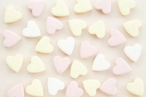 Pattern of yellow pink and white candy hearts on a beige background.. Stock Photos