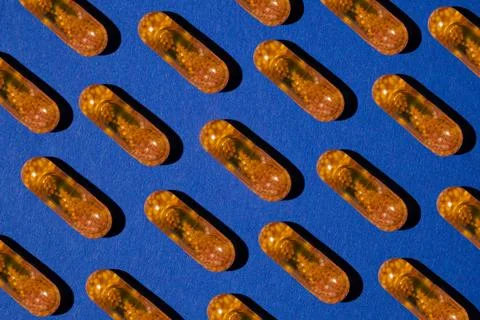 Pattern of yellow transparent liquid capsules with granules on a blue background Stock Photos