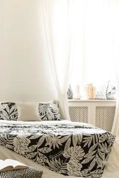 Patterned blanket on bed in bright hotel bedroom interior with white drapes a Stock Photos