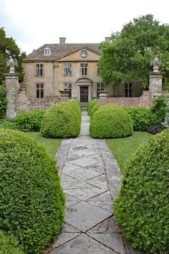 A patterned concrete block walkway between rounded topiary shrubs in an Engli 스톡 사진