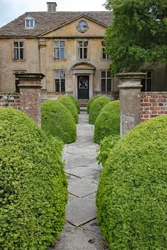 A patterned concrete block walkway between rounded topiary shrubs in an Engli 스톡 사진
