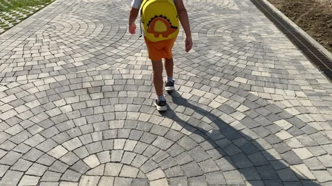 Patterned Path: Young Boy with Dinosaur Backpack Walks on Cobblestone Street Stock Footage 318317998