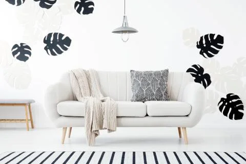 Patterned pillow and blanket on sofa in white living room interior with monst Stock Photos