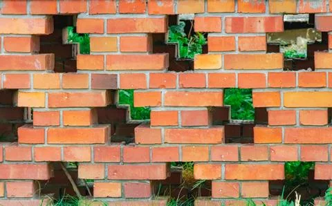 Patterned red brick wall with intentional gaps revealing green grass and pl.. Stock Photos