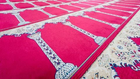 Patterned red prayer carpets arranged across mosque floor Stock Photos