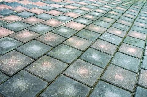 A patterned sidewalk of worn square pavers features contrasting dark and li.. Stock Photos
