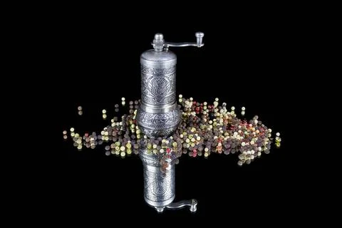 Patterned silver pepper mill and pepper balls scattered around on black Stock Photos