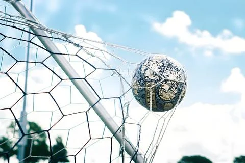 Patterned Soccer Ball Hitting Goal Net Against Blue Sky Foto stock