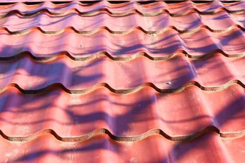 Patterns of sunlight casting shadows on a vibrant red tiled roof in a warm .. Stock Photos