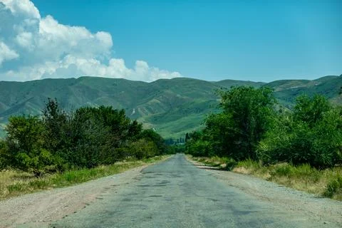 Paved mountain road winding through green hills under dramatic sky Kyrgyzstan Stock Photos