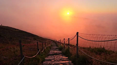 Paved mountain trail with chain fence in pink sunset fog. Stock Footage 340339965