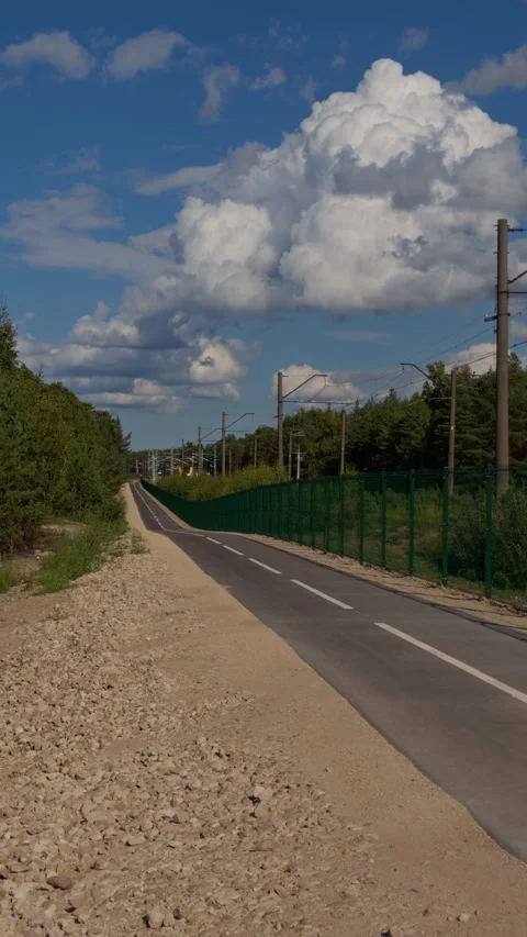 Paved path beside railway corridor under dramatic cumulus clouds with forest Stock Footage 345454064
