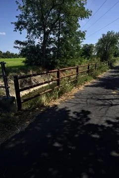 Paved path next to a creek and a field bordered by trees on a sunny day in .. Stock Photos