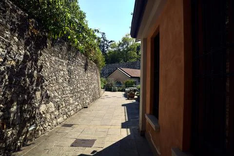 Paved path in a park between a stone wall and a building on a sunny day Fotos de archivo