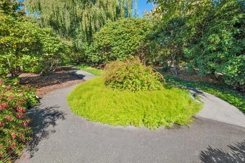 Paved pathway through a park with round flowerbed in the middle Stock Photos