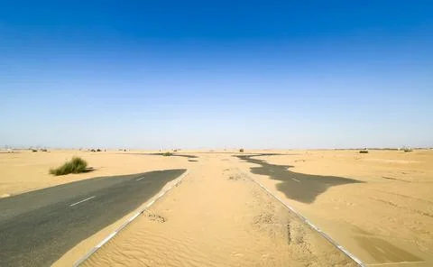 A paved road cuts through the sand dunes of the desert under a bright blue sk Stock Photos