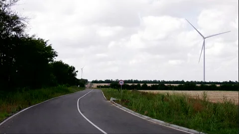 A paved road next to a field with eco-wind turbines and trees Stock Footage 324766691
